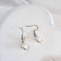 White button-shaped freshwater pearl drop earrings on silver-tone shepherd ear hooks.