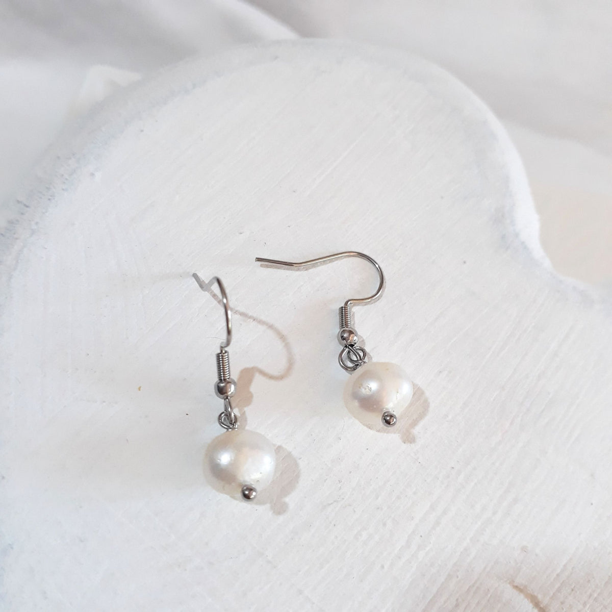 White button-shaped freshwater pearl drop earrings on silver-tone shepherd ear hooks.