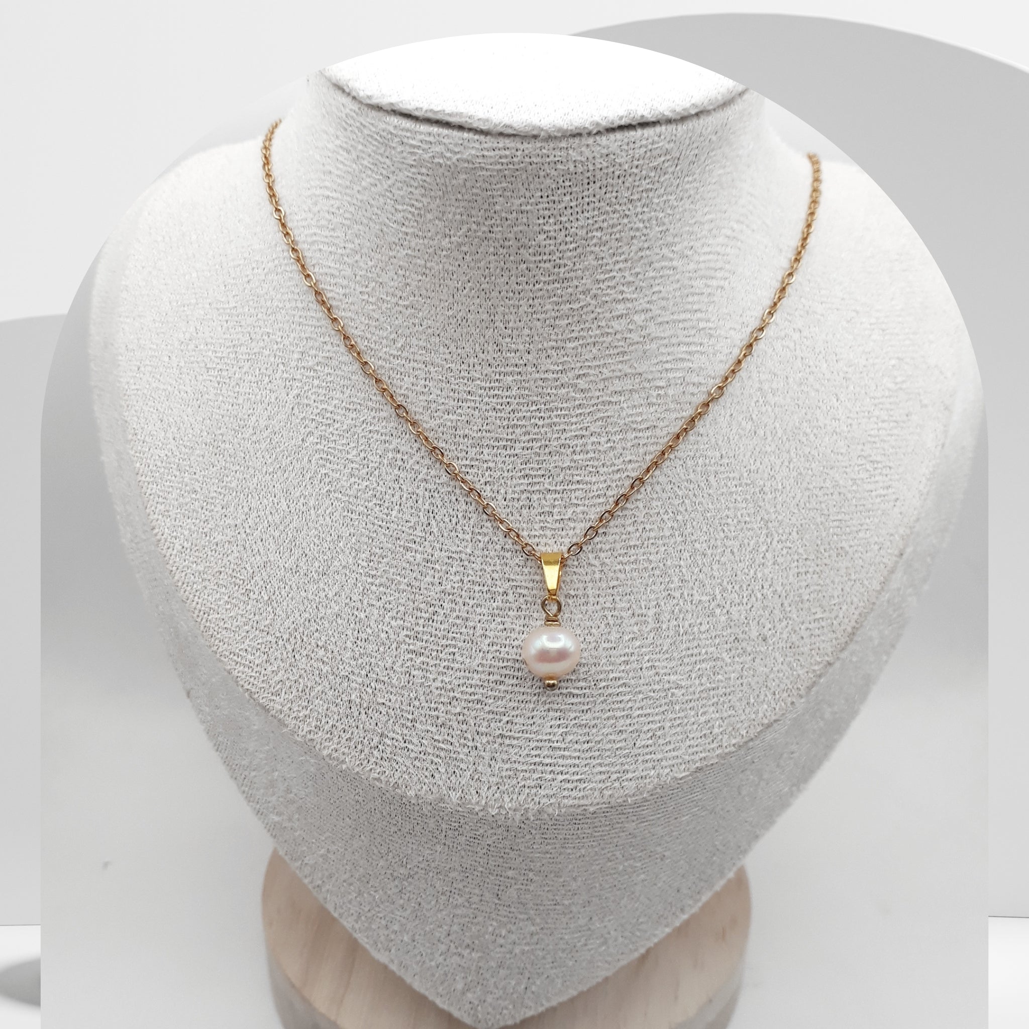 Gold necklace with a pearl pendant on a mannequin bust.