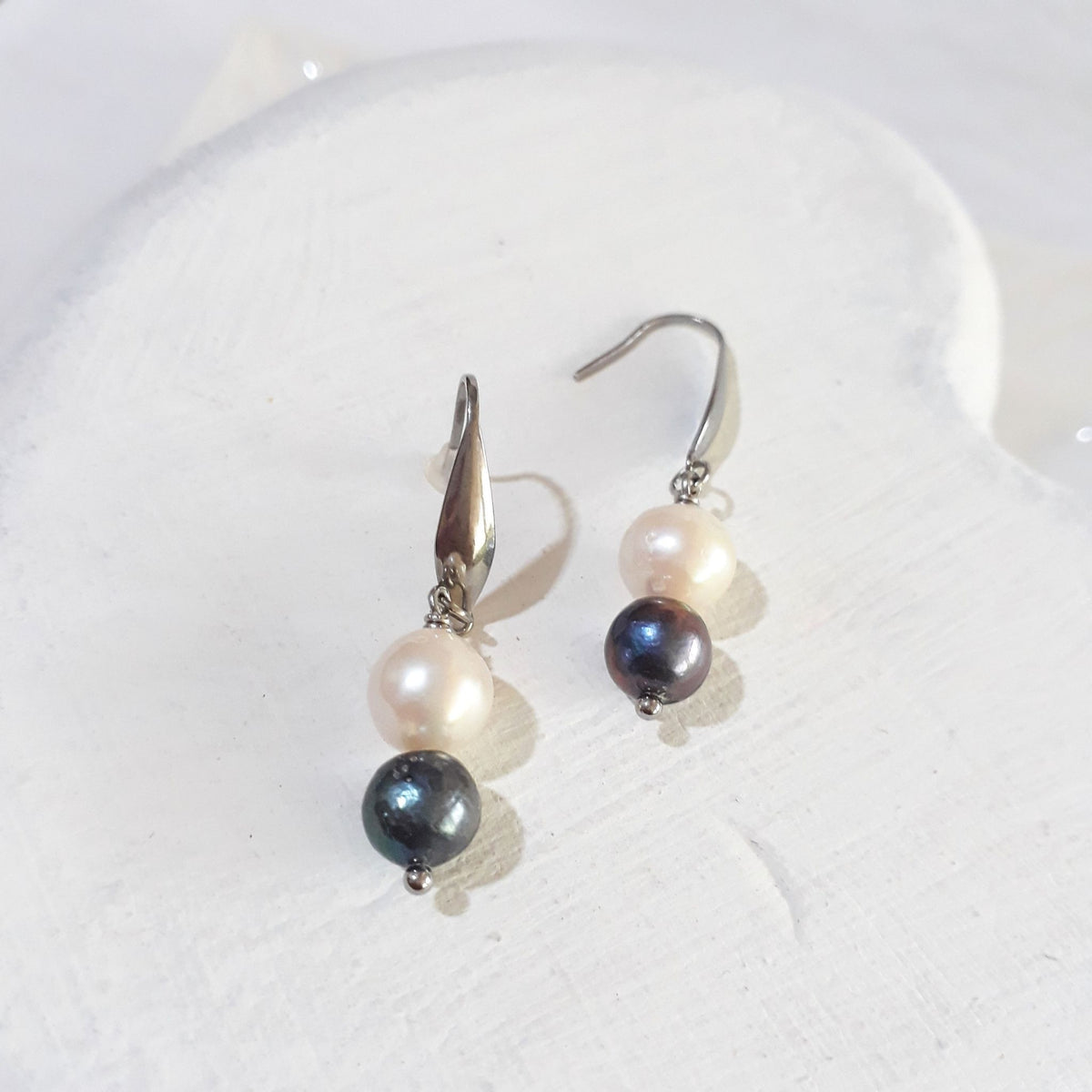 White freshwater pearls above smaller dark peacock pearls with blue-green highlights on silver-tone elegant ear hooks.