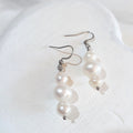 White button freshwater pearls between smaller white semi-baroque pearls on silver-tone shepherd ear hooks.