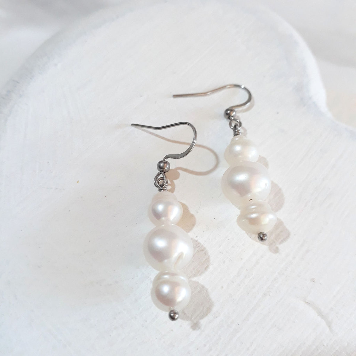 White button freshwater pearls between smaller white semi-baroque pearls on silver-tone shepherd ear hooks.