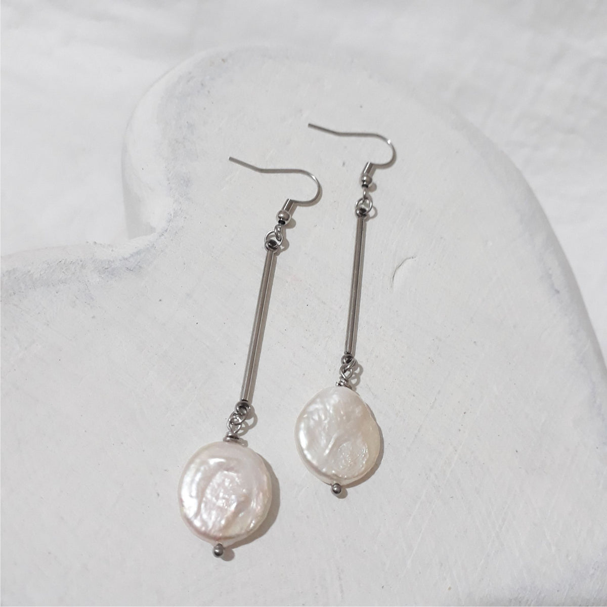 White freshwater coin pearl dangle earrings with slender stainless steel bars and shepherd hooks.