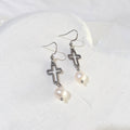 White freshwater pearls hanging beneath open silver-tone crosses on ear hooks, displayed on a white background.