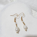 White pear-shaped freshwater pearl earrings with small rice pearls, white ceramic heart connectors and gold-tone shepherd hooks.