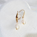 White pear-shaped freshwater pearls beneath tiny white rice pearls on gold-tone elegant ear hooks.