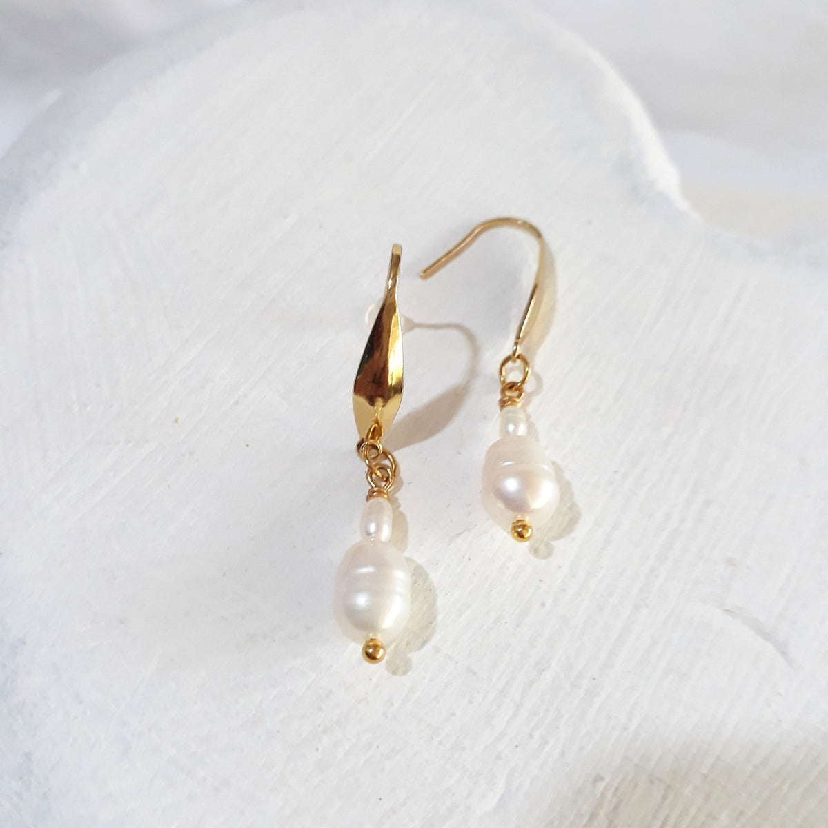 White pear-shaped freshwater pearls beneath tiny white rice pearls on gold-tone elegant ear hooks.