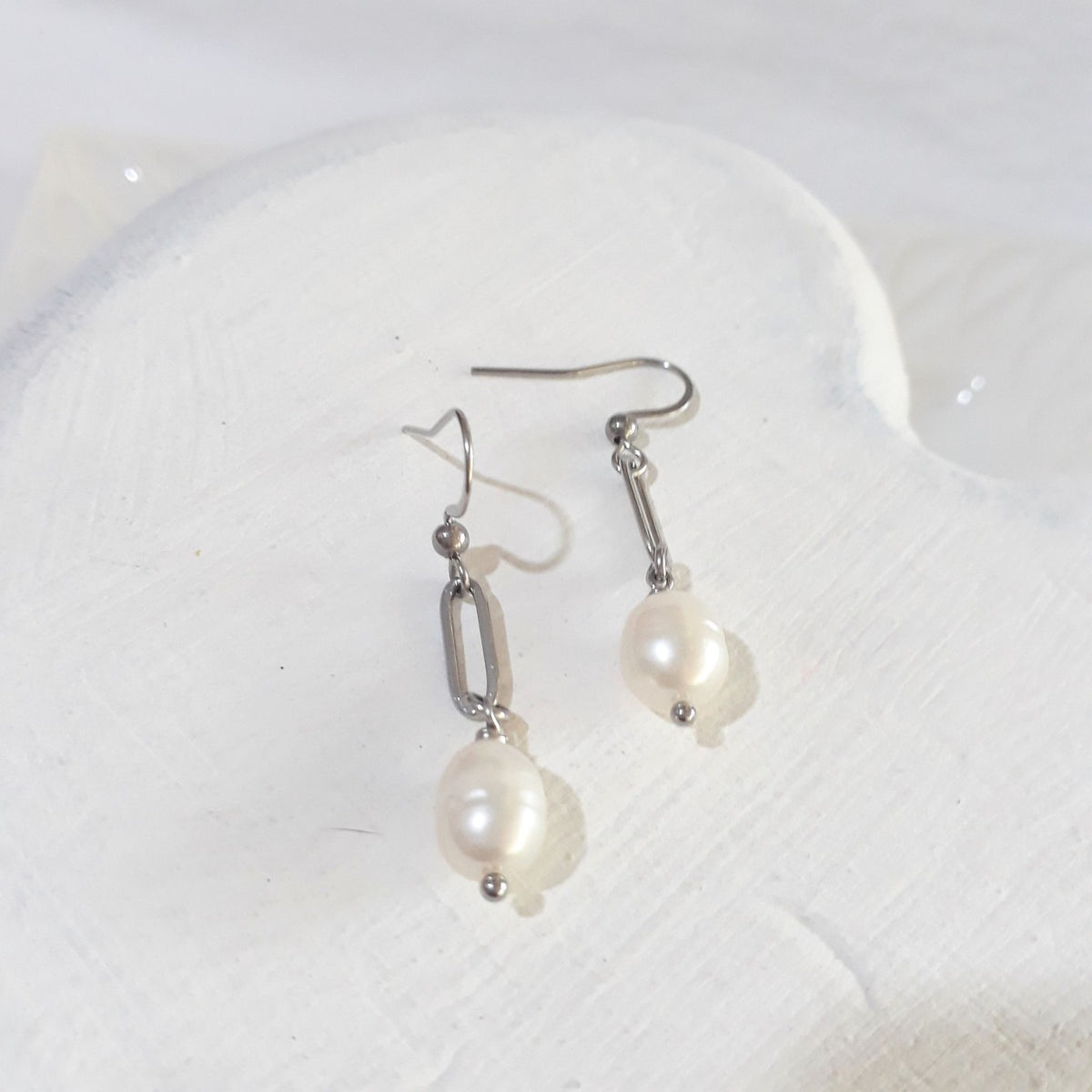 Oval white freshwater pearls suspended beneath silver-tone paperclip links on ear hooks.
