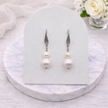 Pearl earrings on a white card with a marble base and flowers in the background