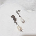 White pear-shaped freshwater pearls beneath small rice pearls and silver-tone oval ear studs with butterfly backs.
