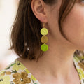 Woman wearing a polymer clay cascade earring in lemon yellow, mustard and green with a gold plated ear hook.