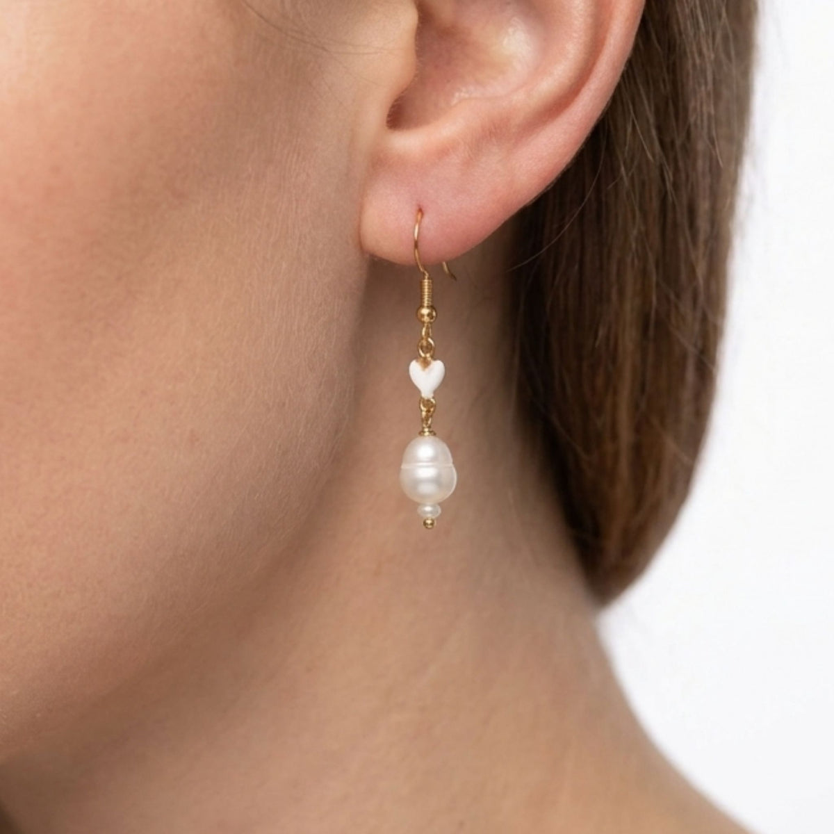 A woman wearing a gold-plated freshwater pearl with a white ceramic heart drop earring.