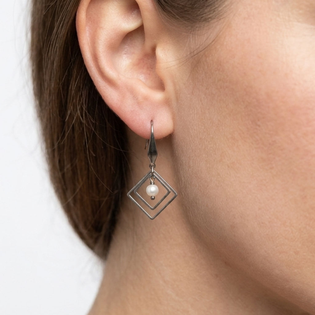 Close-up of a woman wearing a stainless steel double diamond-shaped dangle earring with a white freshwater pearl.