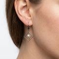 Close-up of a woman wearing a stainless steel double diamond-shaped dangle earring with a white freshwater pearl.