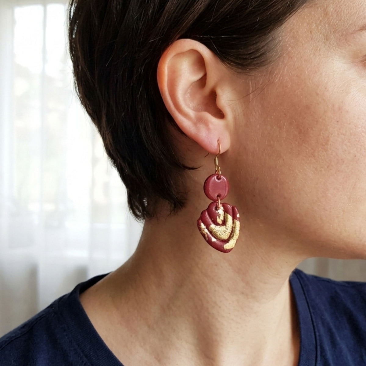 A close-up of a person's ear and neck wearing a dangling dark maroon with gold leaf earring. 