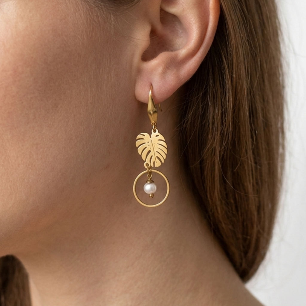 Close-up of a woman wearing a gold-plated monstera leaf earring with a white freshwater pearl inside an open circle.