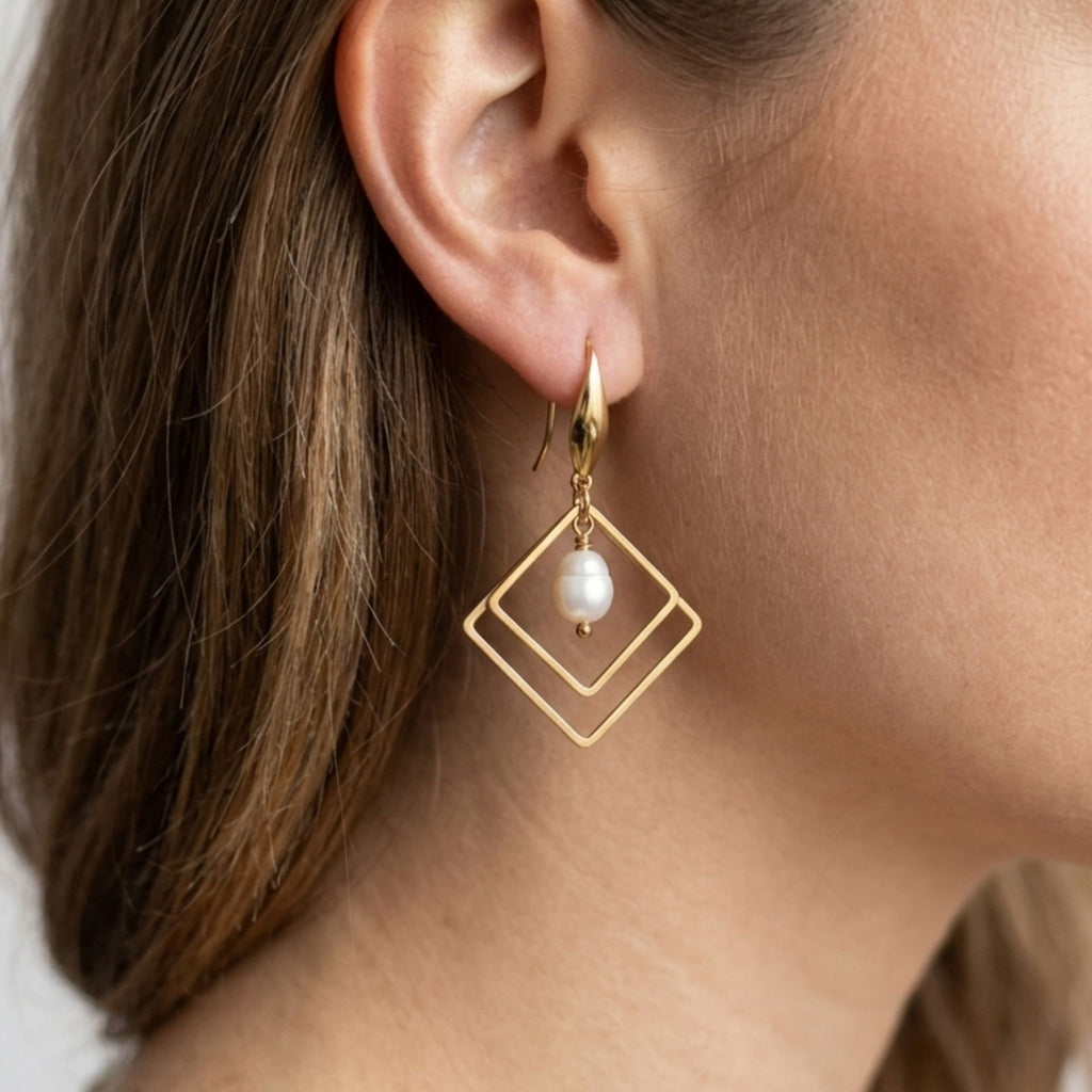Close-up of a woman wearing a gold-plated double diamond-shaped earring with an oval white freshwater pearl.