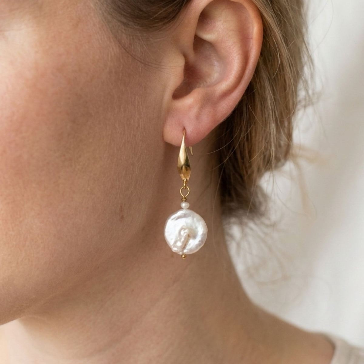 Close-up of a woman wearing a white coin and rice pearl drop earring with a gold-plated elegant hook.
