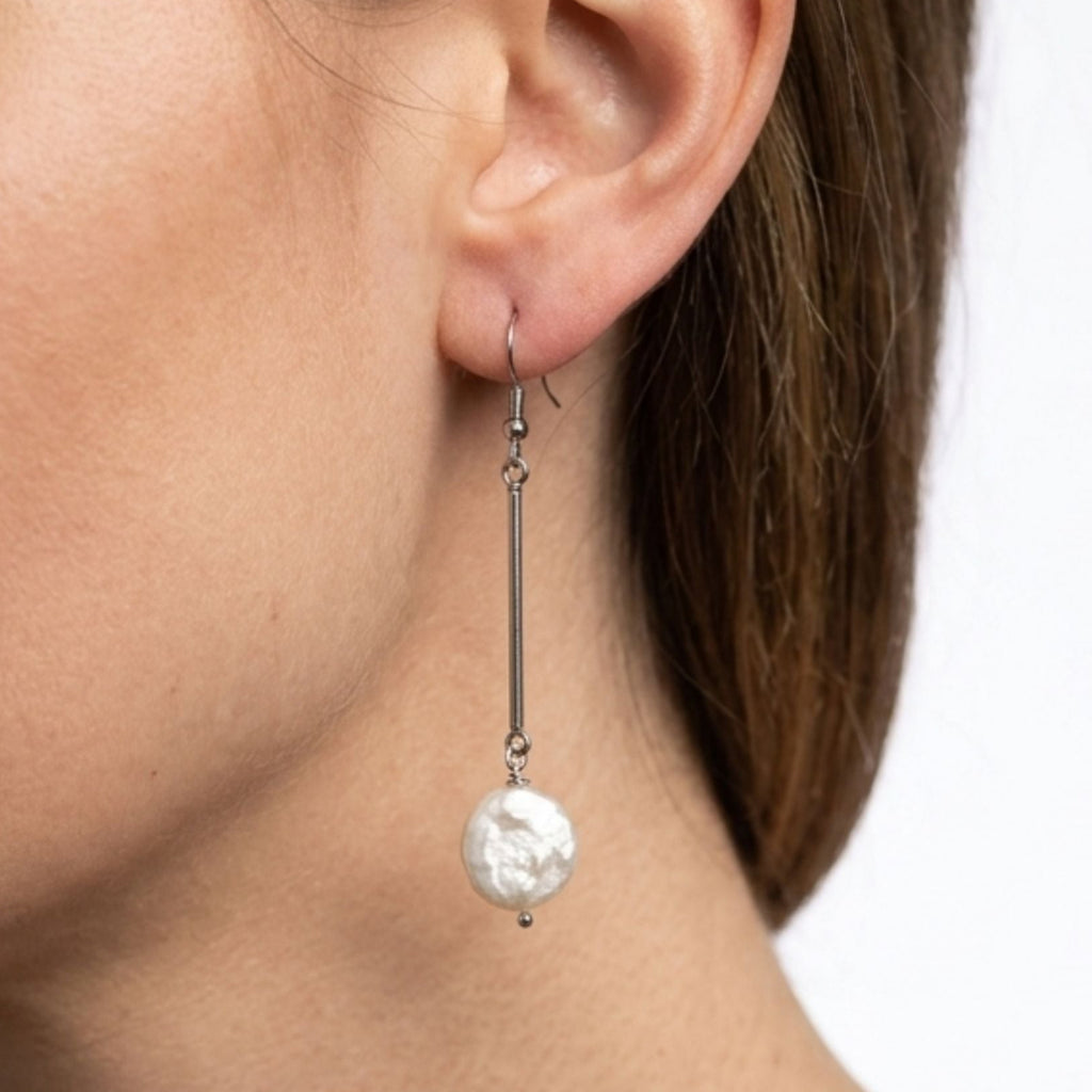 Close-up of a woman wearing a long stainless steel bar earring with a white freshwater coin pearl.