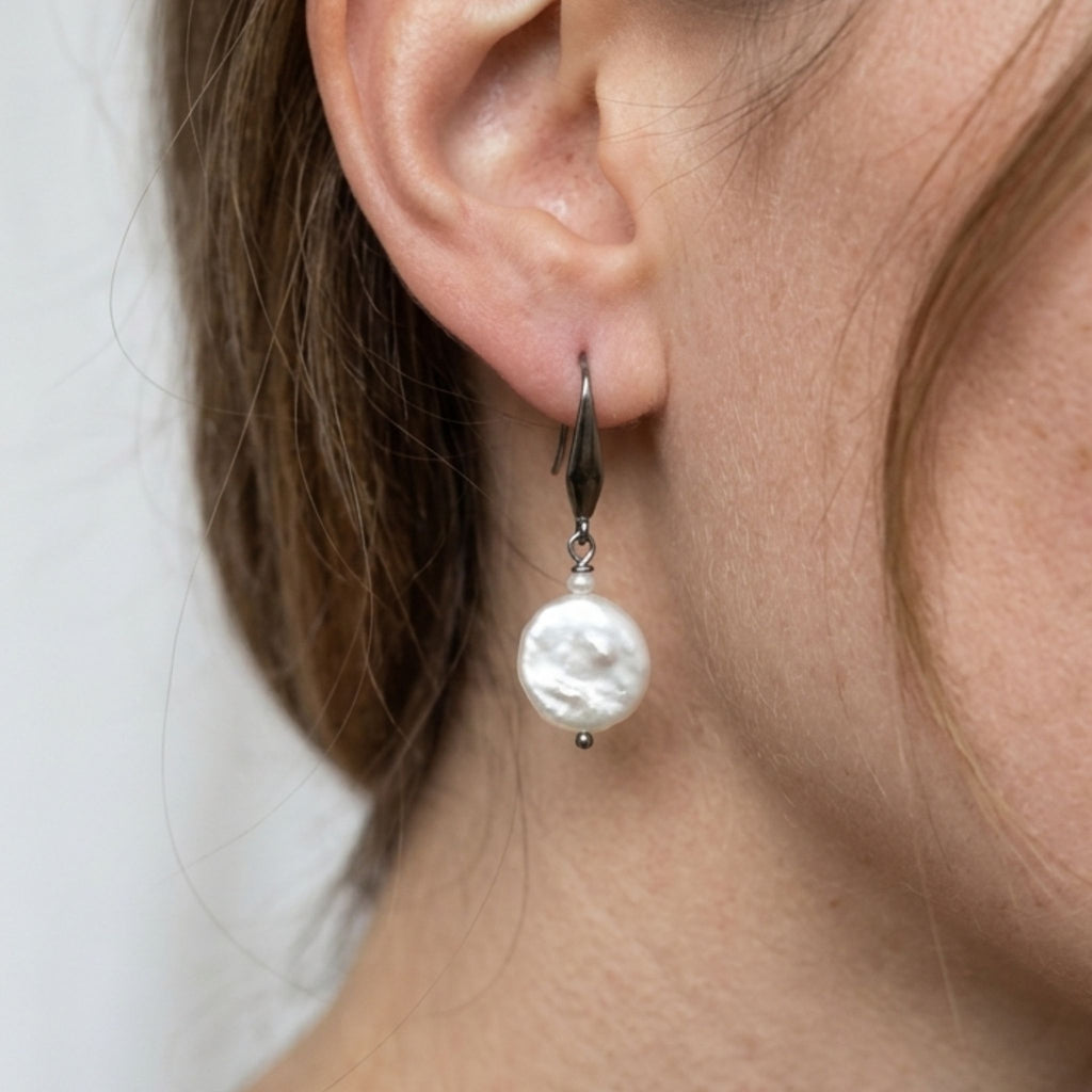Close-up of a woman wearing a white coin and rice pearl drop earring on a stainless steel elegant hook.