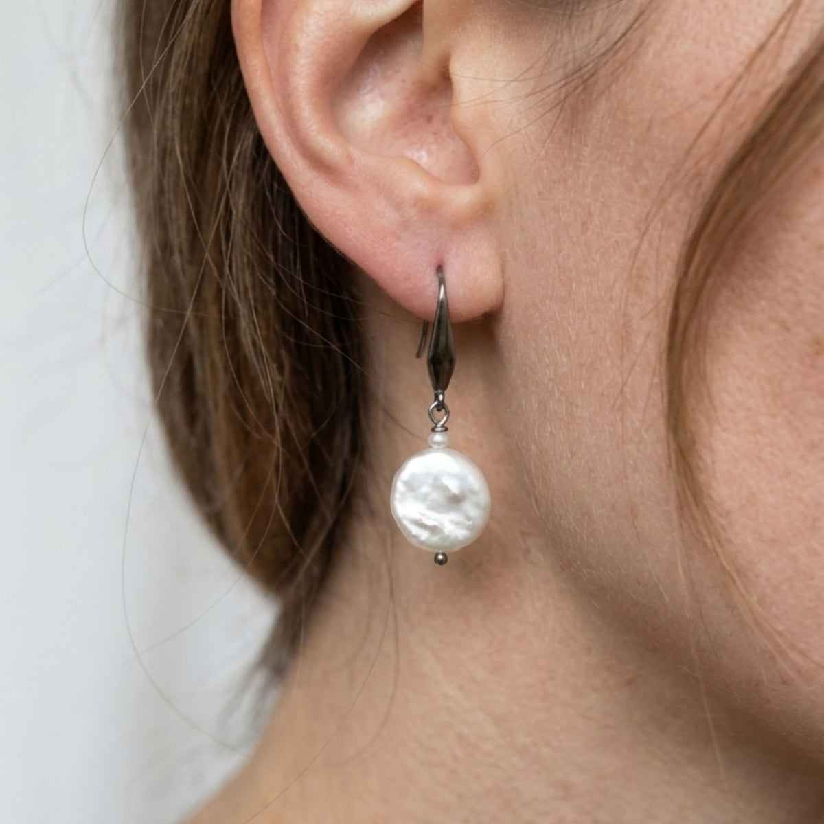 Close-up of a woman wearing a white coin and rice pearl drop earring on a stainless steel elegant hook.