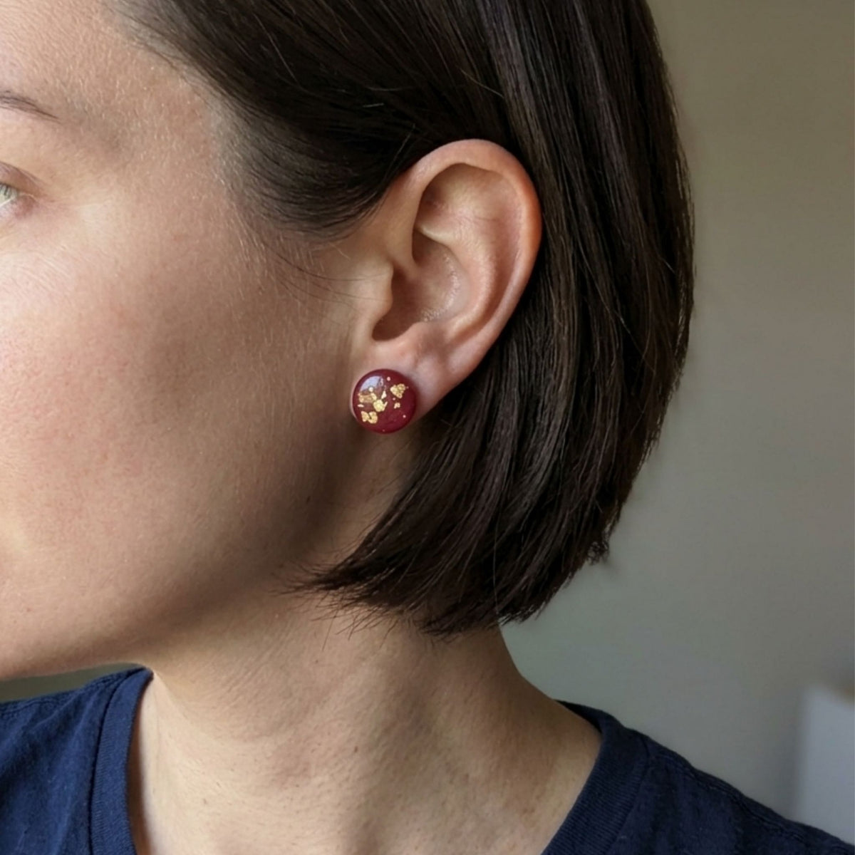 Woman wearing a 14mm round dark maroon handcrafted polymer clay earring with gold leaf.
