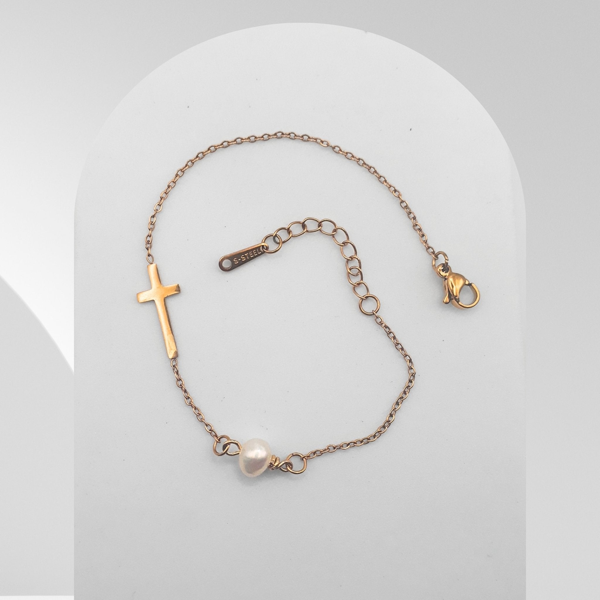 Bracelet with cross charm and pearl on a light gray background