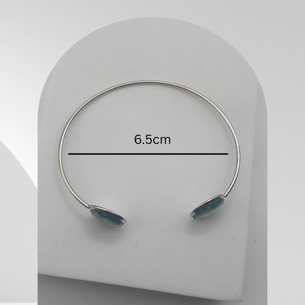 Silver bracelet with green stones on a white stand, showing measurement of 6.5cm.