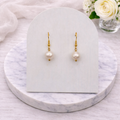 Pearl Gold earrings on a marble stand with a white card and flowers in the background