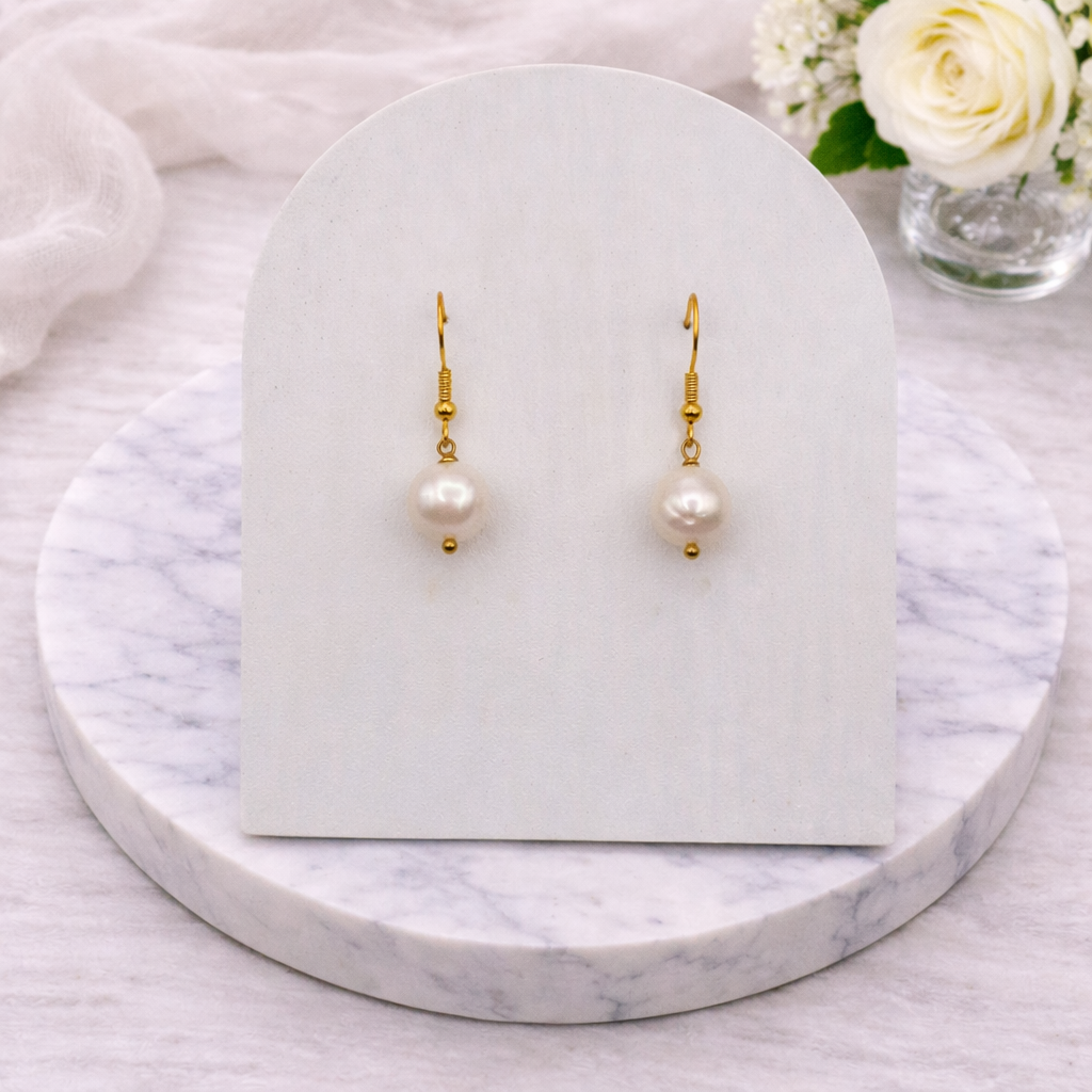 Pearl Gold earrings on a marble stand with a white card and flowers in the background