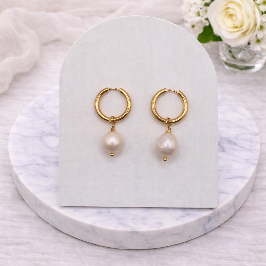 Gold hoop earrings with pearl drops on a white marble surface.