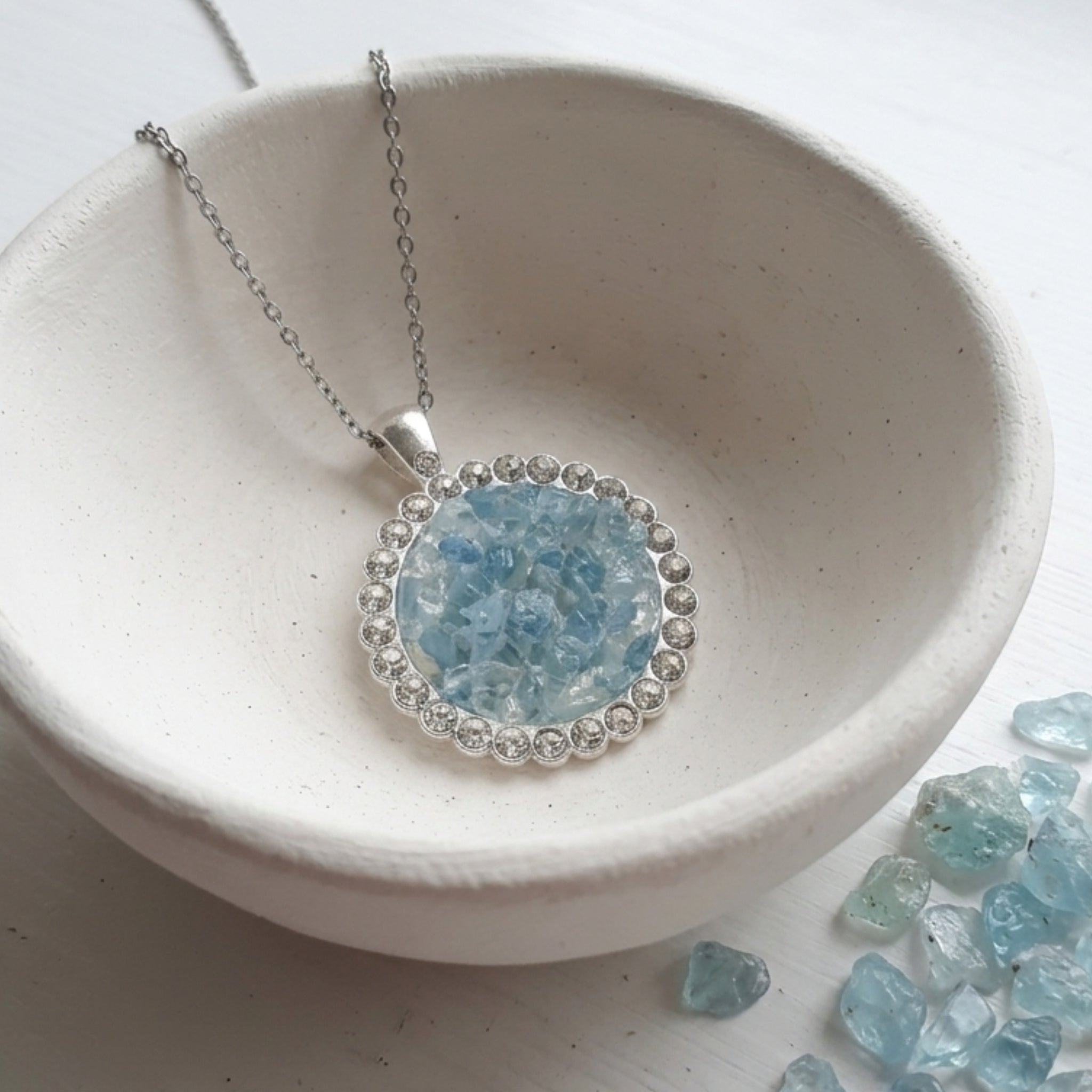 Handmade round aquamarine gemstone pendant necklace with rhinestone border on a stainless steel cable chain.