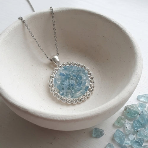 Handmade round aquamarine gemstone pendant necklace with rhinestone border on a stainless steel cable chain.