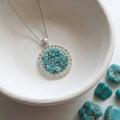 Handmade round turquoise gemstone pendant necklace with rhinestone border on a stainless steel chain.