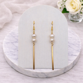 Pair of pearl earrings on a marble stand with flowers in the background