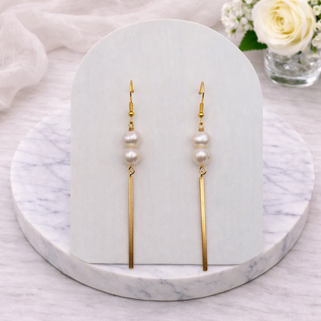 Pair of pearl earrings on a marble stand with flowers in the background