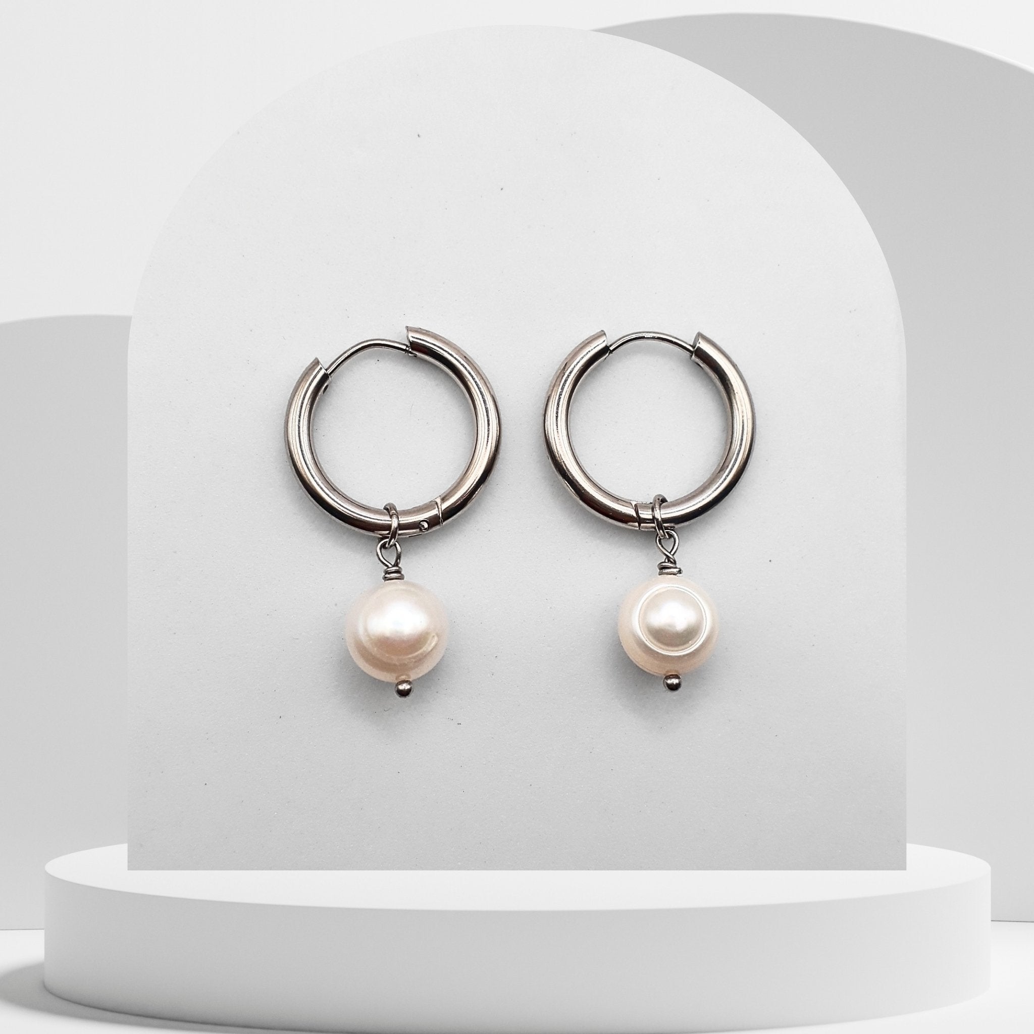 Silver hoop earrings with pearl drops on a white background