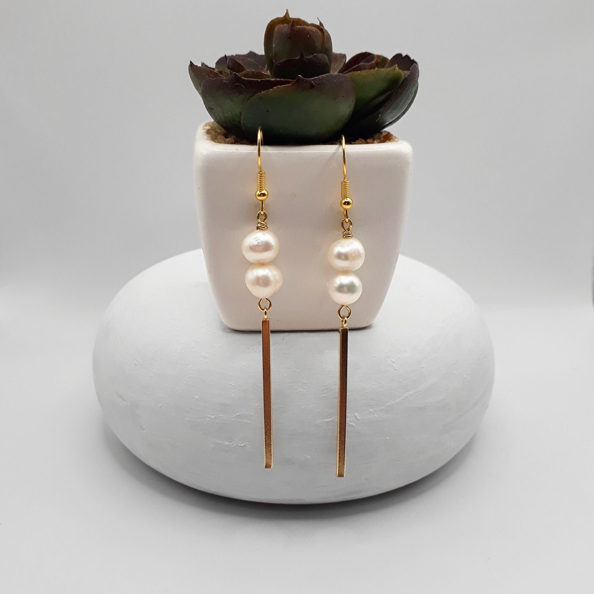 Gold-plated stainless steel freshwater pearl dangle earrings with double pearls and gold bar drops displayed beside a succulent plant.