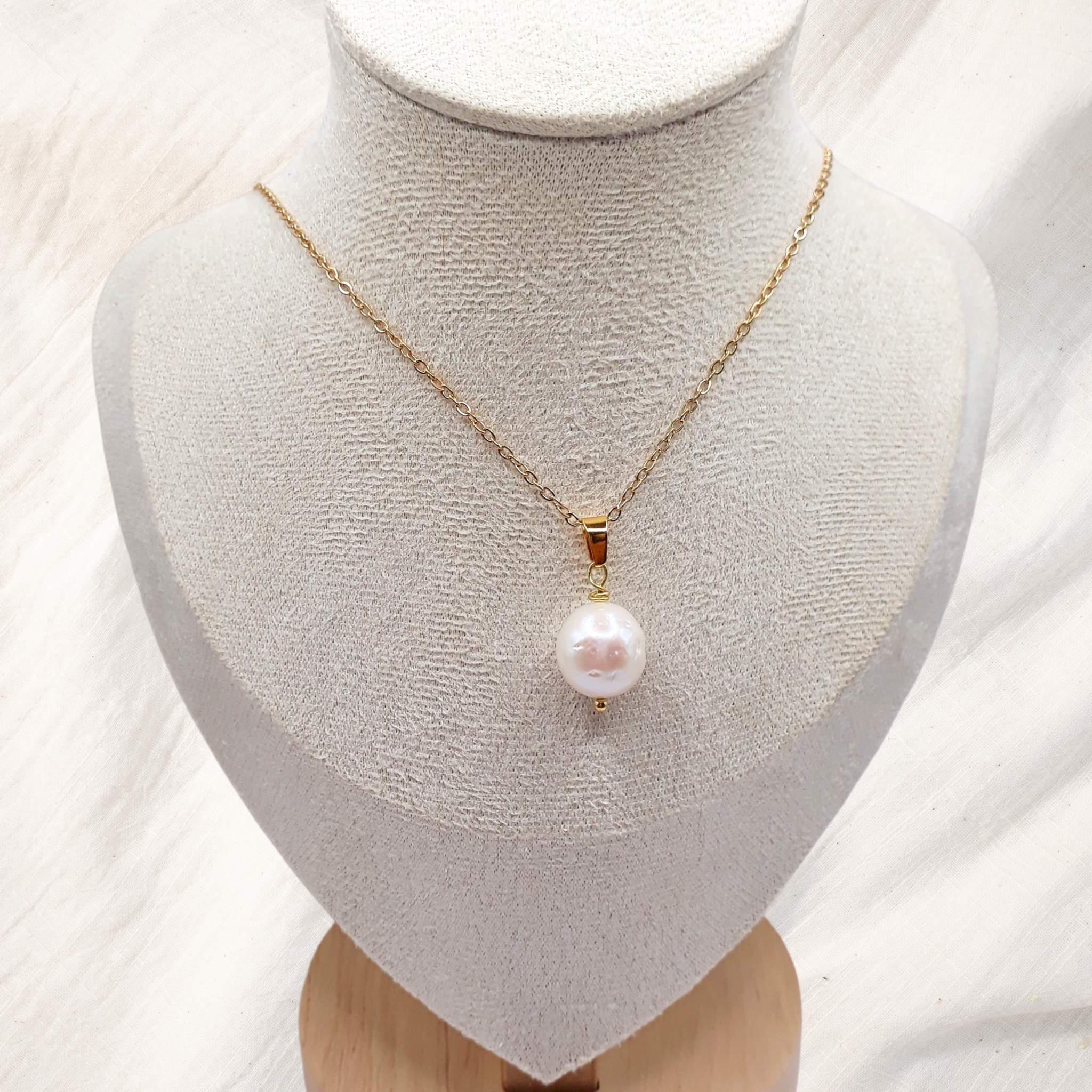 Gold plated stainless steel necklace with an 11 mm white freshwater pearl displayed in front of a succulent planter.