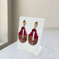 Handmade dark maroon and gold Art Deco arch polymer clay earrings with gold leaf studs on white display stand