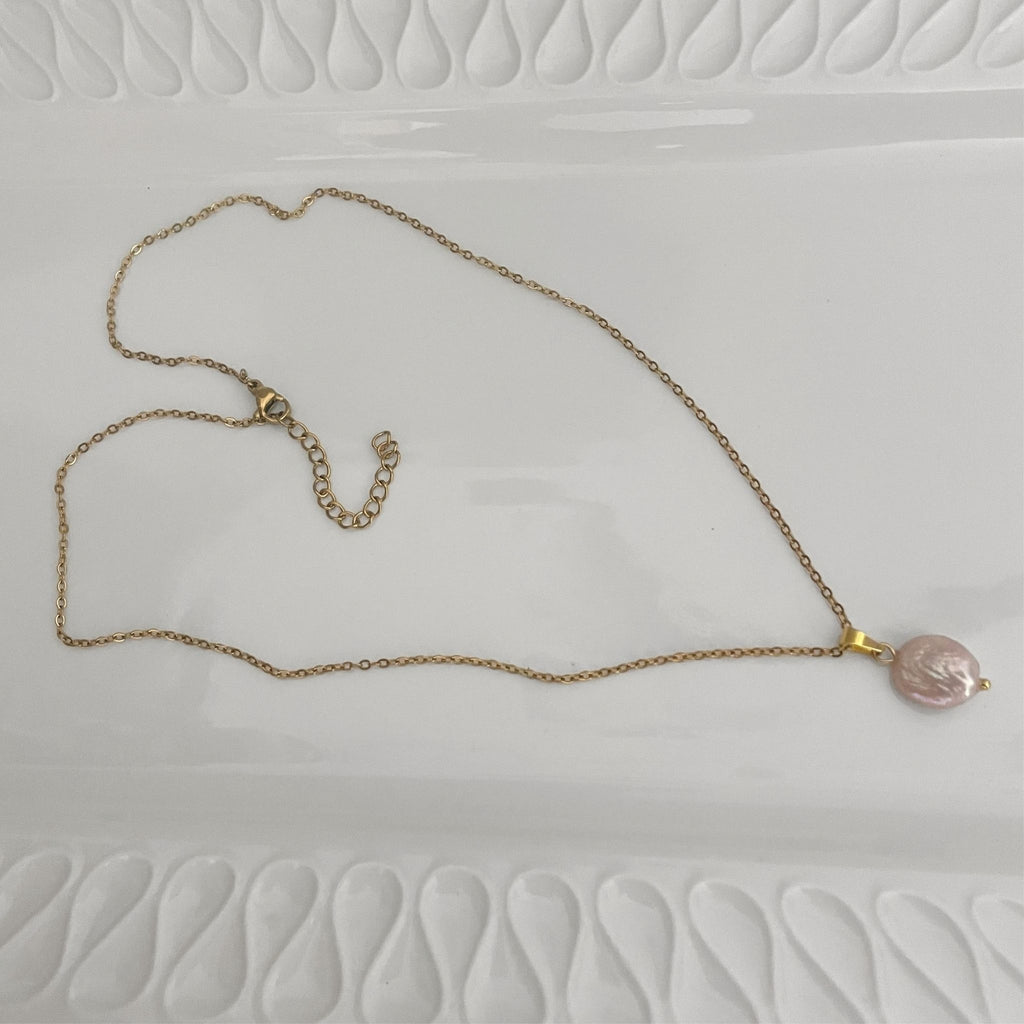 Handmade necklace with a freshwater soft pink coin pearl on a gold-plated chain lying flat on a white ceramic plate.
