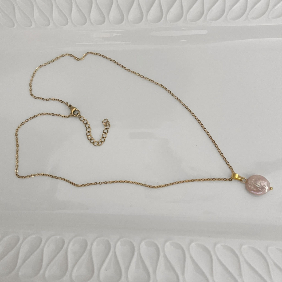Handmade necklace with a freshwater soft pink coin pearl on a gold-plated chain lying flat on a white ceramic plate.