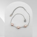 Handmade stainless steel bracelet featuring three soft pink freshwater pearls accented with white rice pearls on a cable chain.