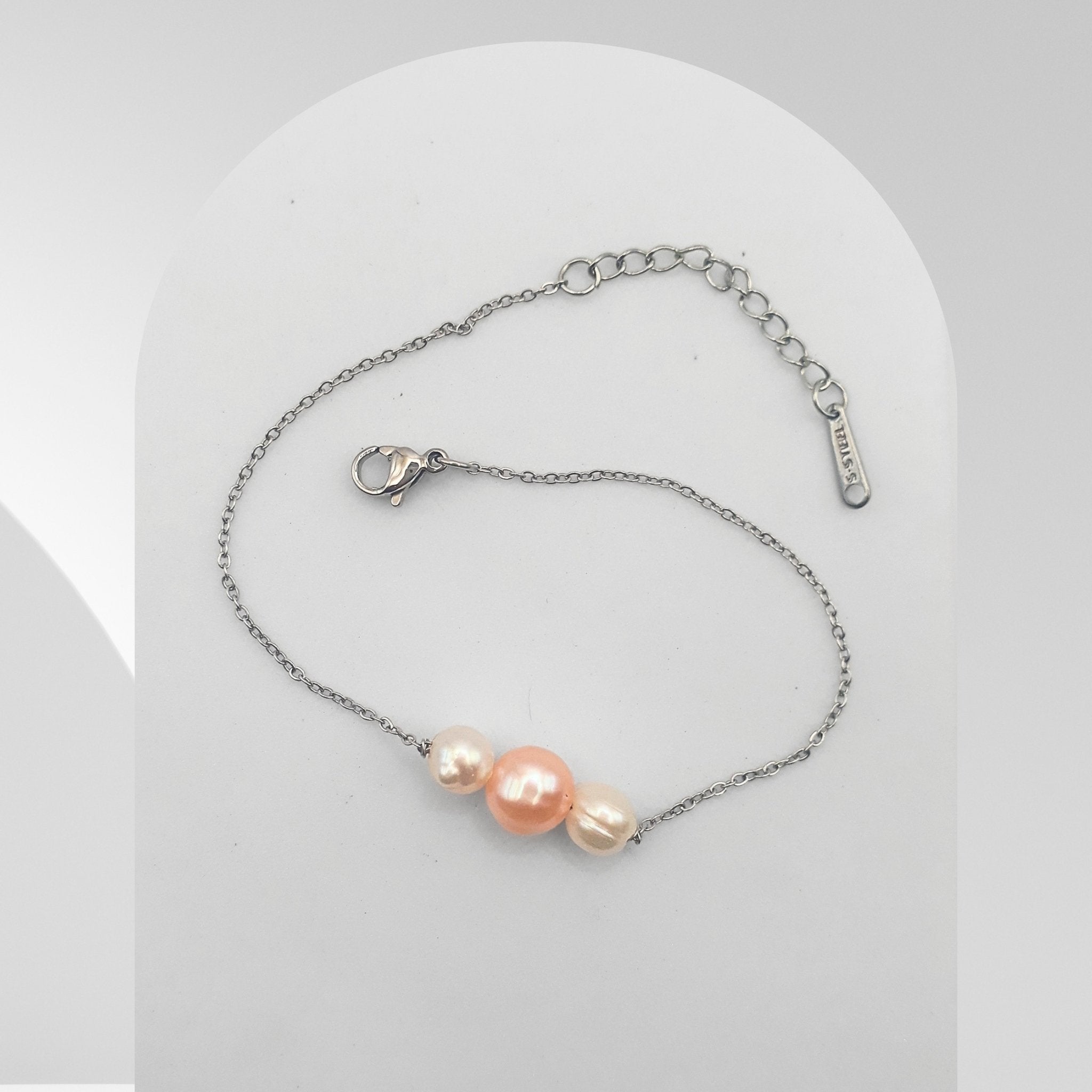 Handmade stainless steel bracelet featuring a peach-pink freshwater pearl with two peach-white freshwater pearls on a cable chain.