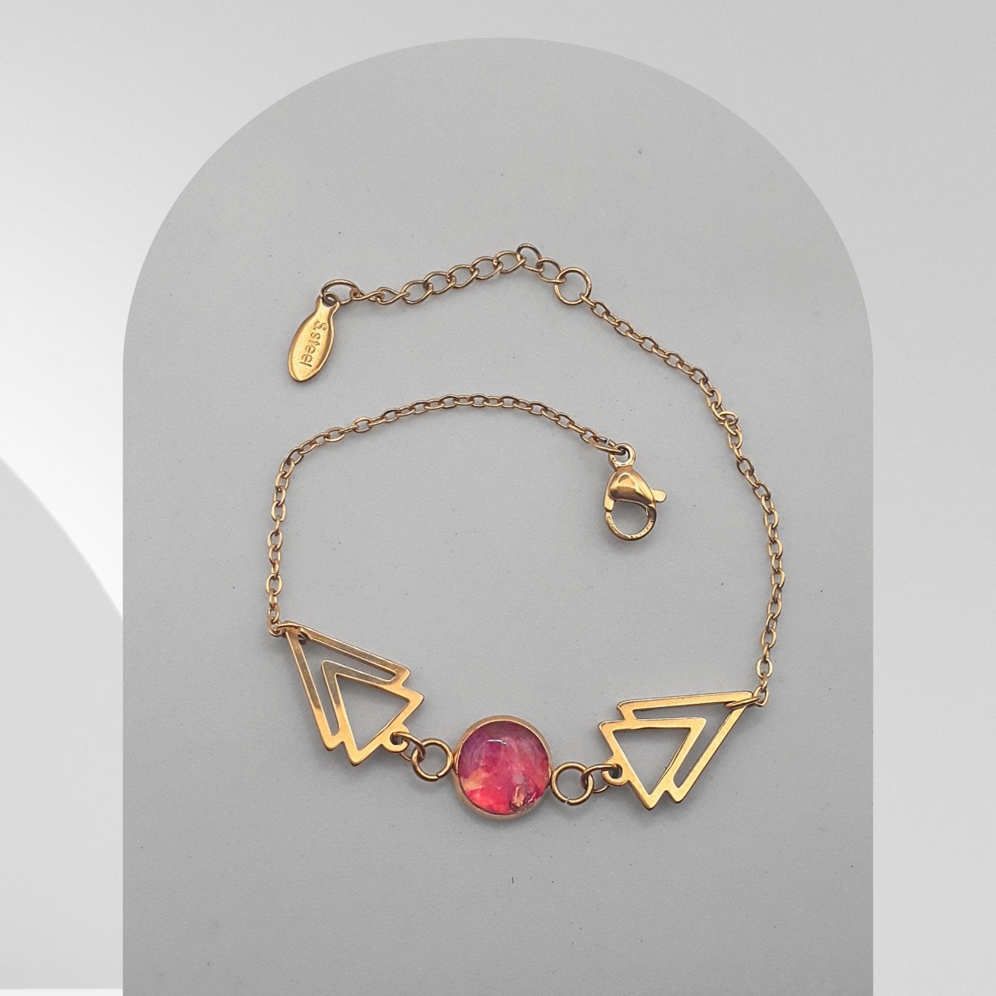 Gold bracelet with geometric designs and a pink gemstone on a gray background