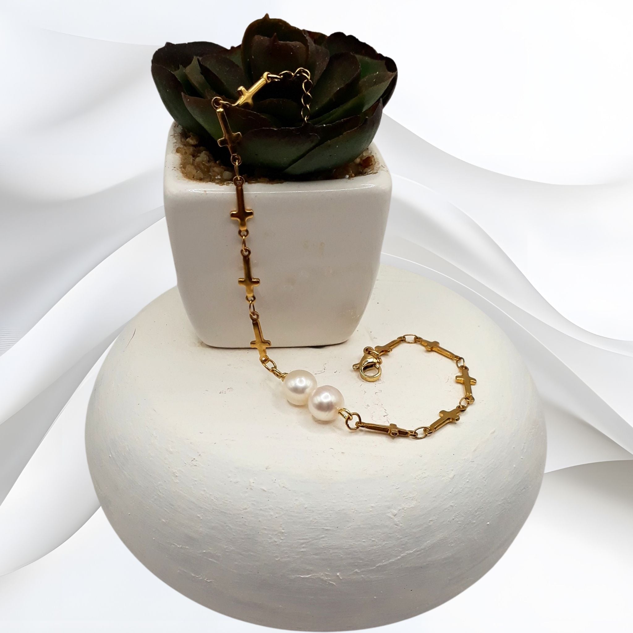 Gold bracelet with pearls on a white surface next to a small plant in a white pot.