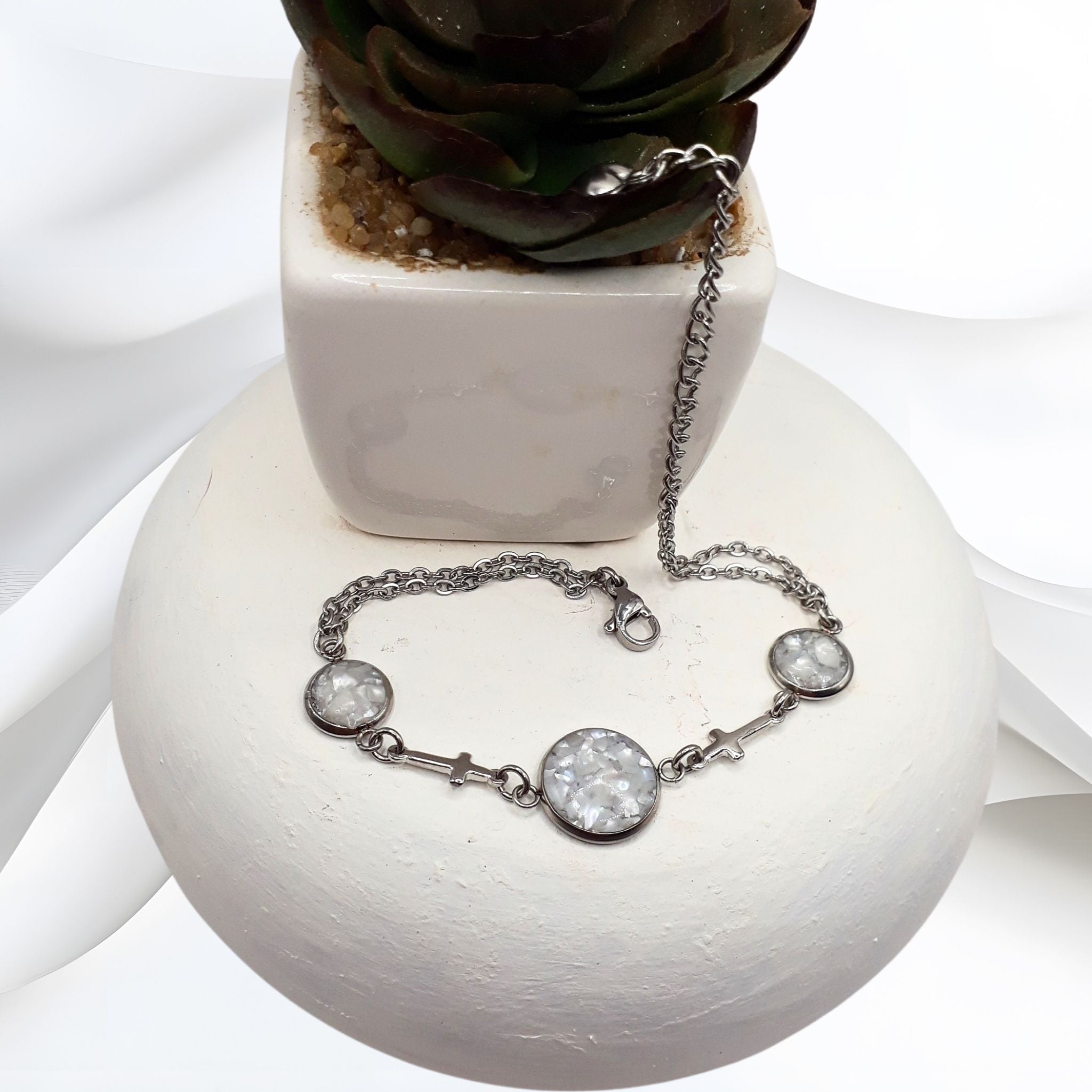 Silver bracelet with gemstones on a white surface with a plant in the background