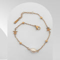 Gold bracelet with star and pearl charm on a light gray background