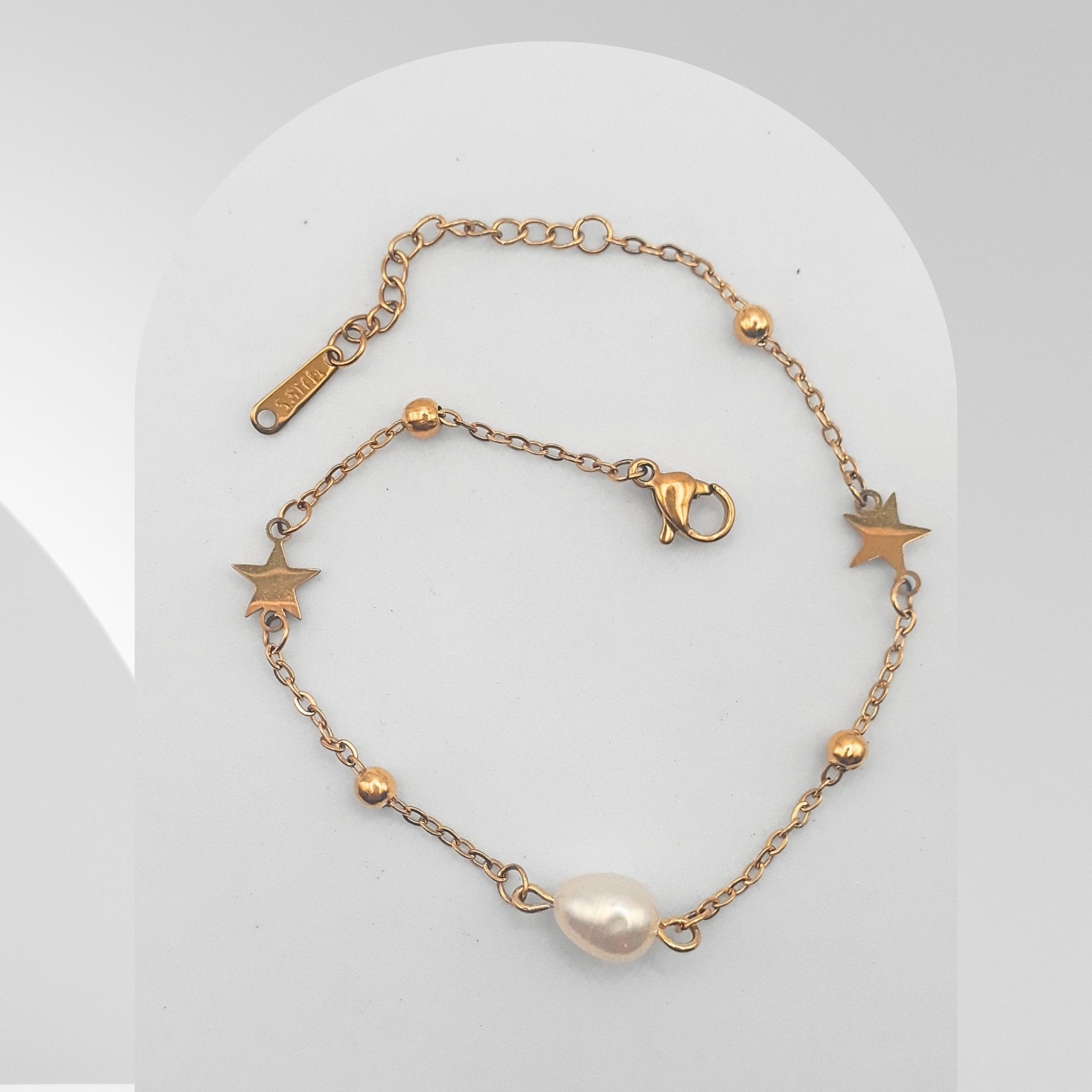 Gold bracelet with star and pearl charm on a light gray background