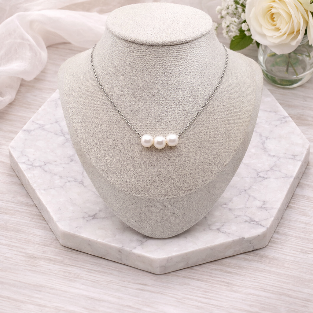 Pearl necklace on a gray bust with white roses in the background